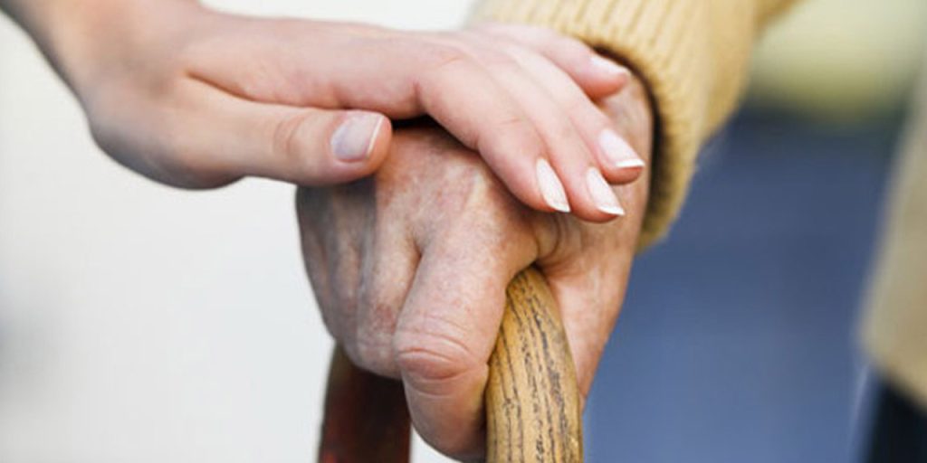 someone holding an elderly persons hand who's using a wooden walking stick